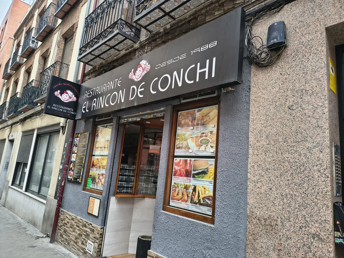 Fachada del restaurante con el rótulo El Rincón de Conchi y fotos de platos en las ventanas