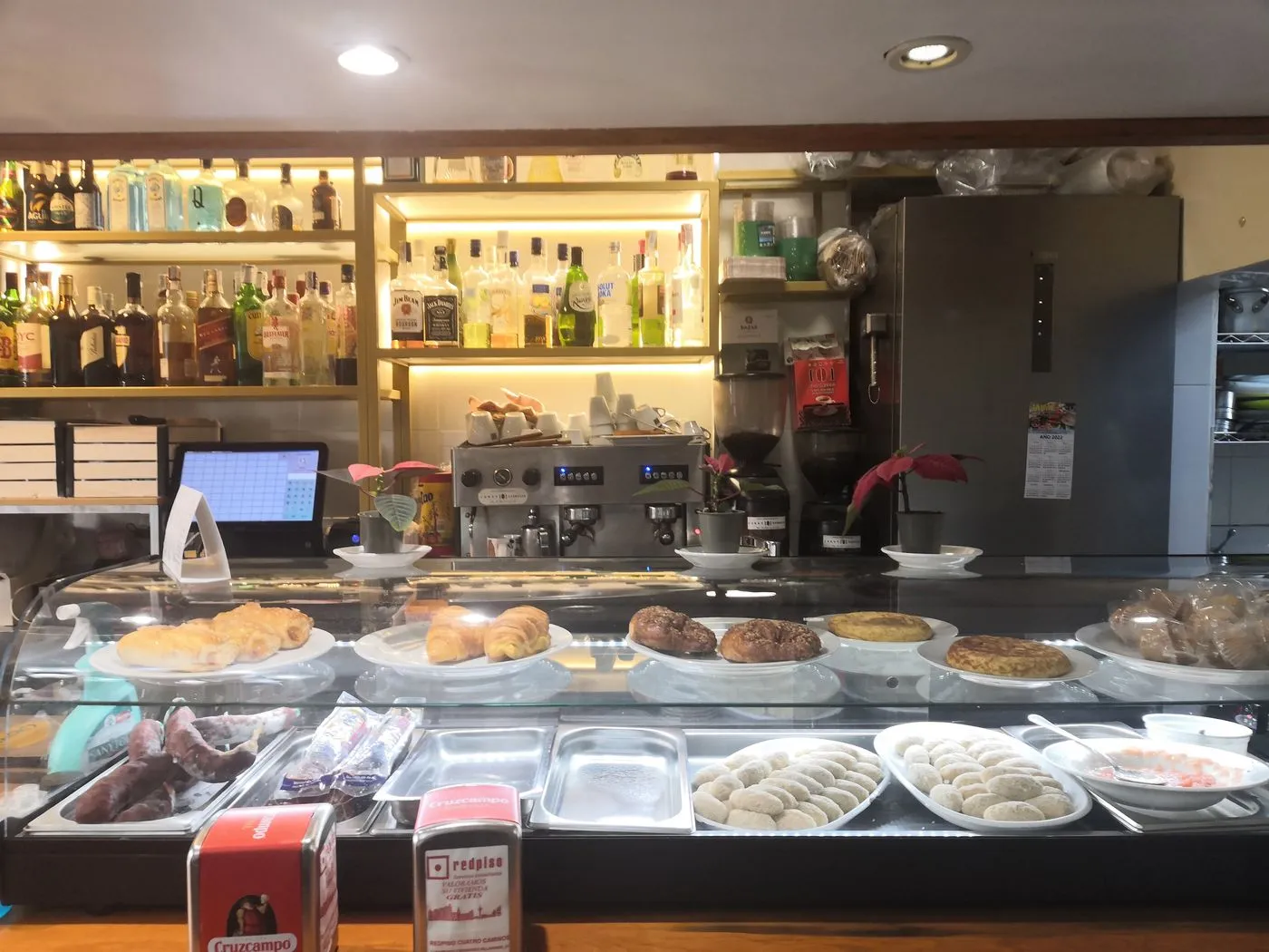 Barra con vitrina de bollería, tortillas y croquetas, y botellas en las estanterías