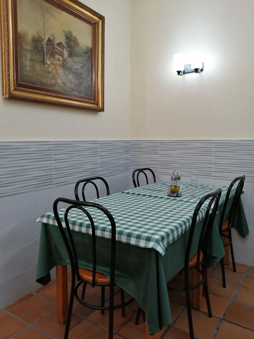 Mesa con mantel de cuadros verdes y cuatro sillas negras junto a un cuadro de paisaje